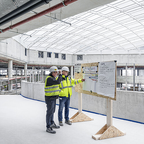 Planer in Warnwestern vor einem Reißbrett im Rohbau des FIZ von BMW in München